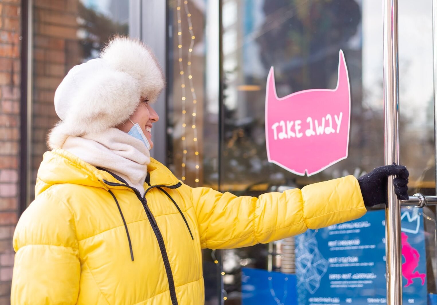 Happy young woman at the door of the restaurant on a cold winter day, lettering, takeaway food.